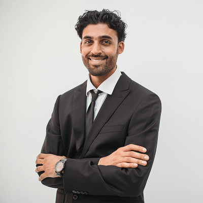Portrait d’un jeune homme souriant en costume sombre, bras croisés, posé devant un mur clair, illustrant la confiance, le professionnalisme et l’élégance.