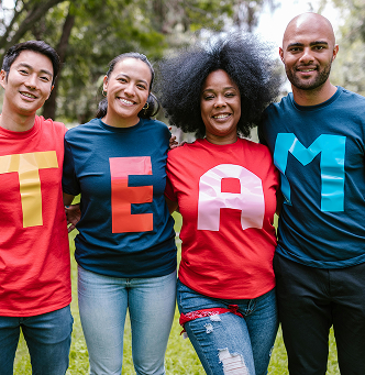 Quatre personnes posant bras dessus bras dessous, portant des t-shirts colorés formant le mot “TEAM”, souriants dans un cadre verdoyant, illustrant la cohésion et la diversité.